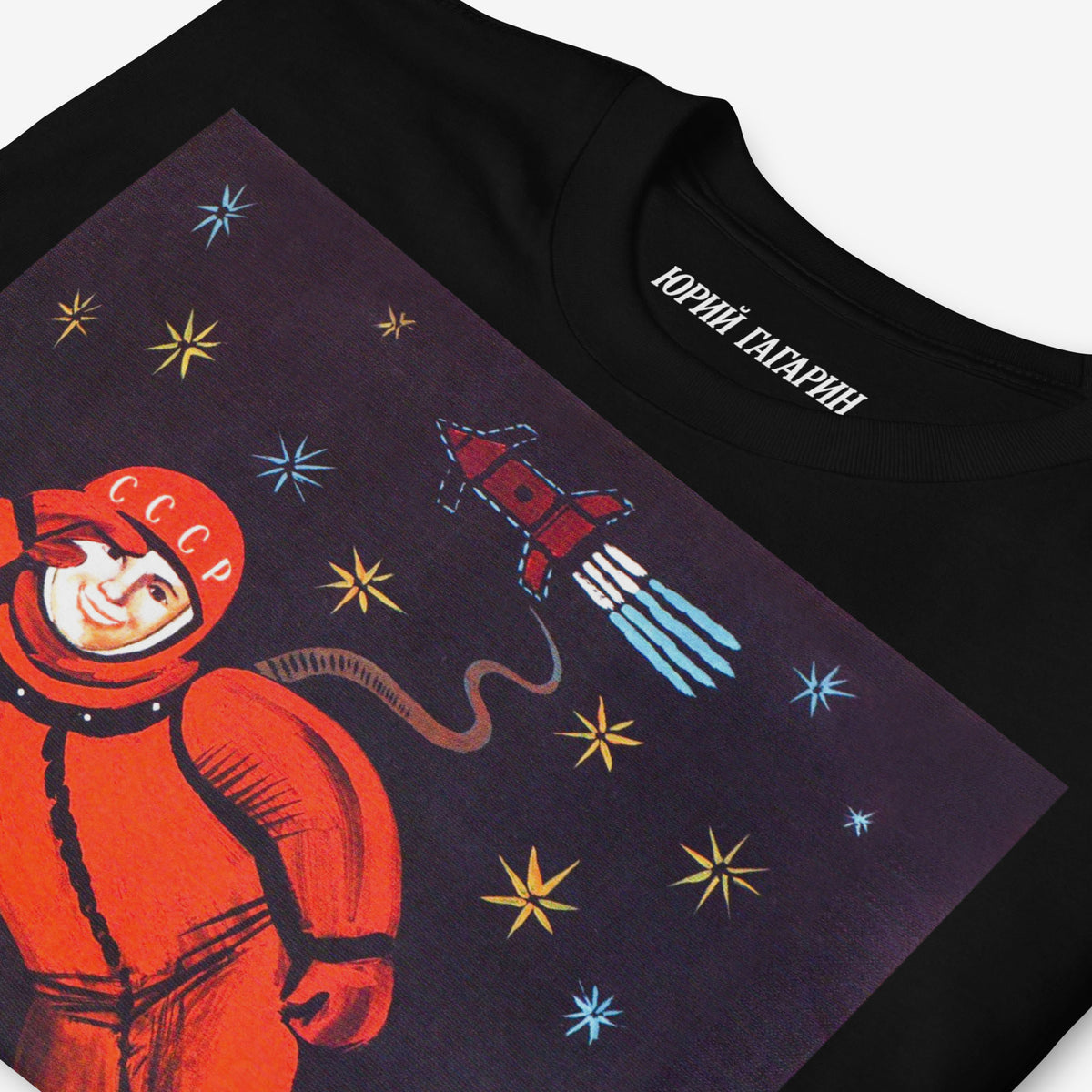 Black unisex T-shirt featuring the iconic Yuri Gagarin floating in space above Russian Orthodox Christian churches and text 'Бога нет' (There's no god). Closeup with 'Юрий Гагарин' logo on the necktag