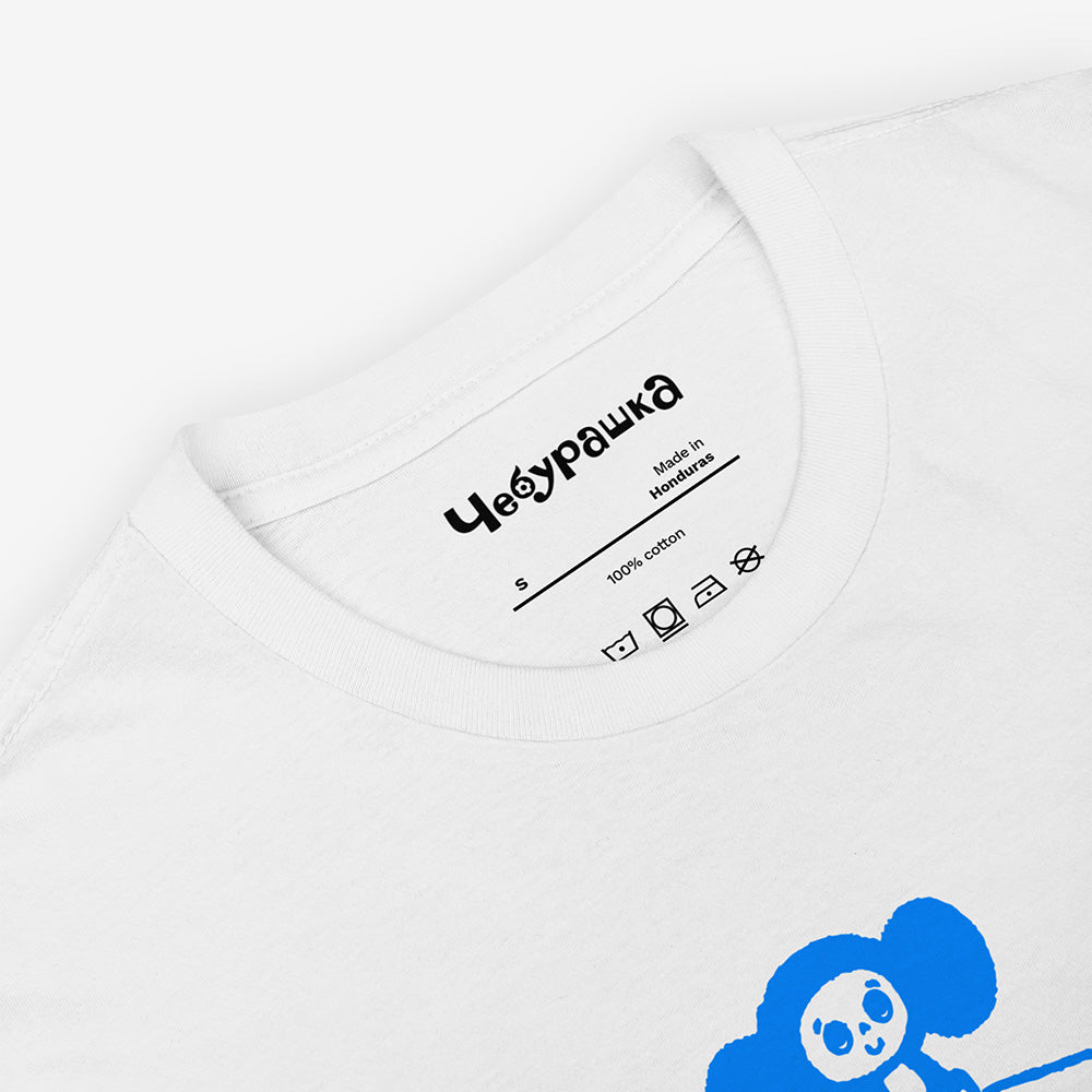 Unisex white Cheburashka T-shirt with a cartoon print of Cheburashka sitting on a box of oranges and チェブラーシカ logo in Japanese.