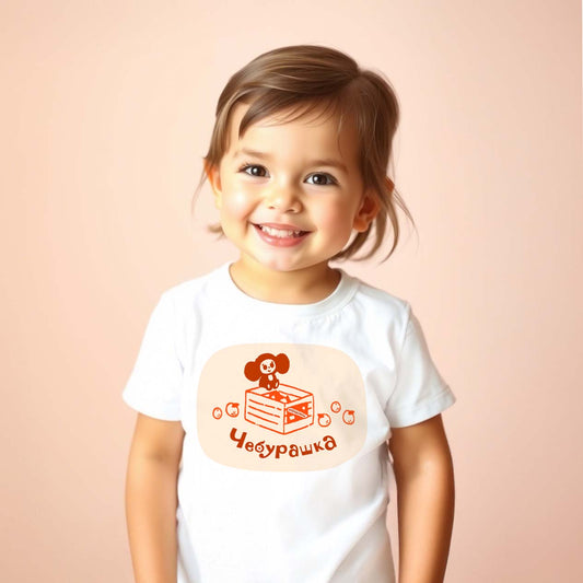 Cute baby girl wearing Cheburashka baby T-shirt featuring the classic Soviet cartoon character sitting on a crate of oranges, inspired by vintage USSR animation.