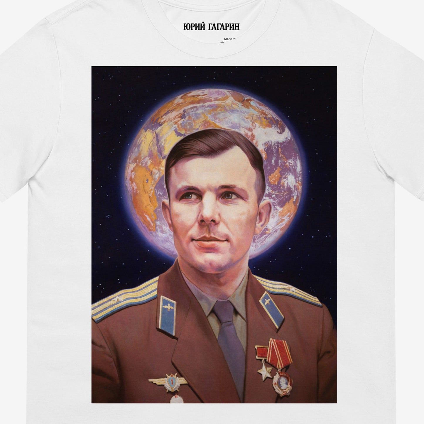 White unisex T-shirt with large painting of Yuri Gagarin in medals, Earth halo behind head. Soviet space icon with Orthodox inspiration. Closeup print details photo with Юрий Гагарин logo in Cyrillic seen on the necktag. www.artsoviet.com