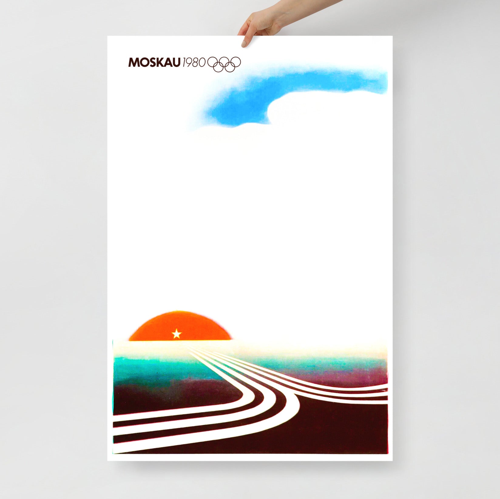 A white skinned hand holds large Moscow 1980 Olympic Games poster with text MOSCAU, Olympic logo and minimalist composition with rising sun and roads made of Moscow Olympics logo going towards it. From artsoviet.com