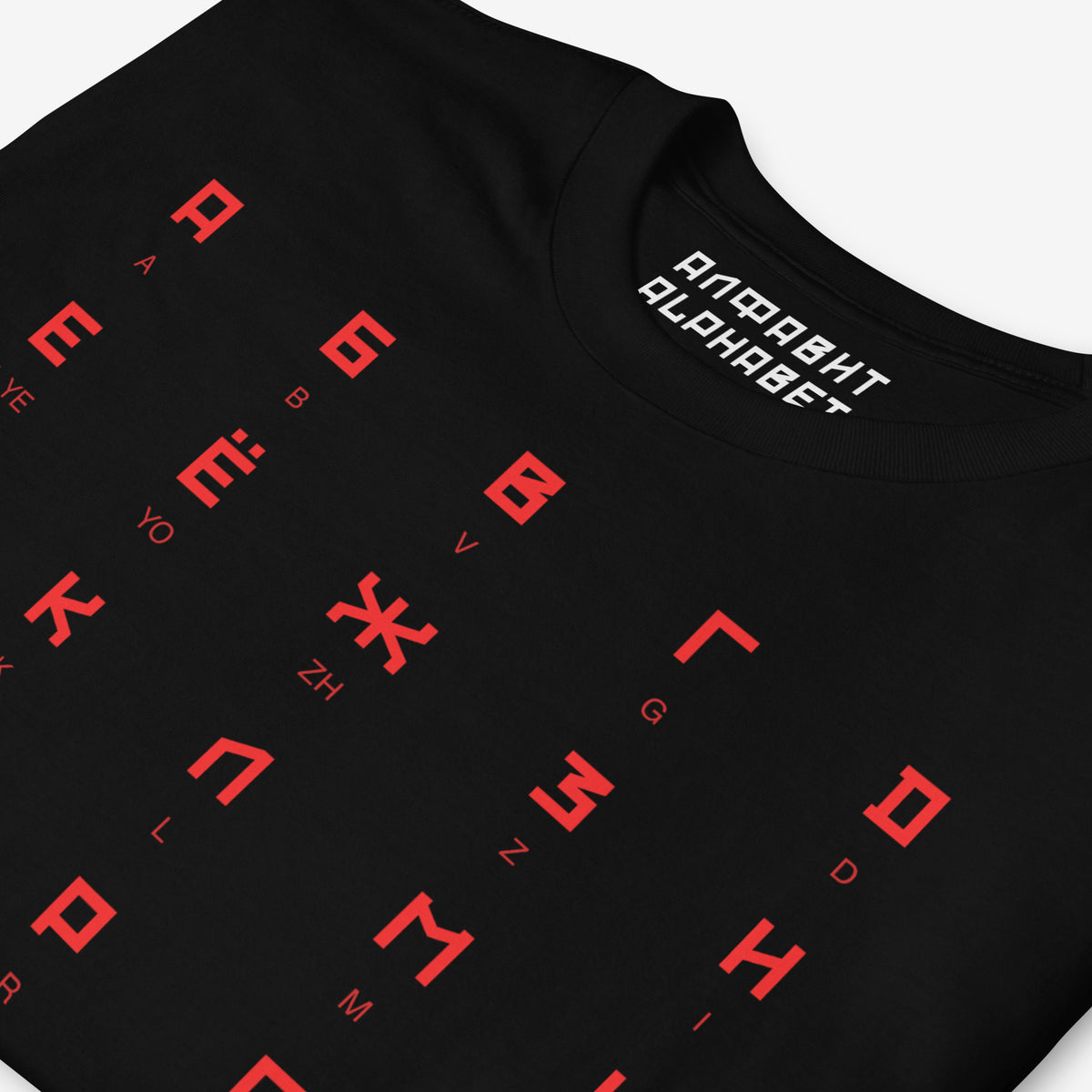 Black Tee featuring large Russian alphabet in a bold Soviet-style font. With english pronunciation beneath each letter. Closeup