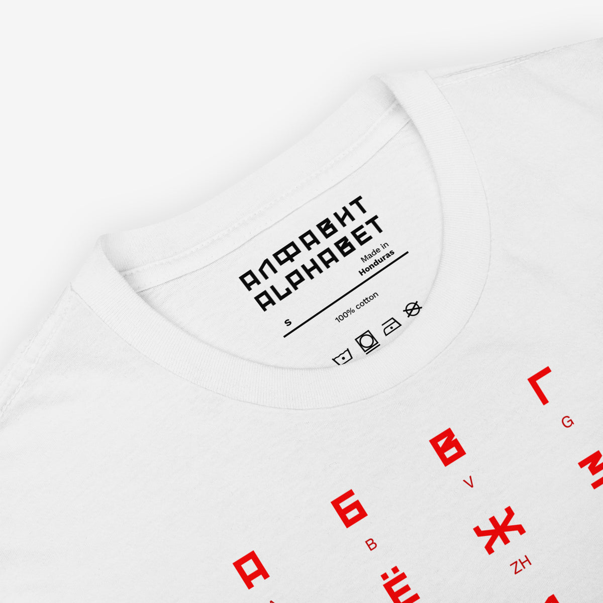White Tee featuring large Russian alphabet in a bold Soviet-style font. With english pronunciation beneath each letter. Closeup
