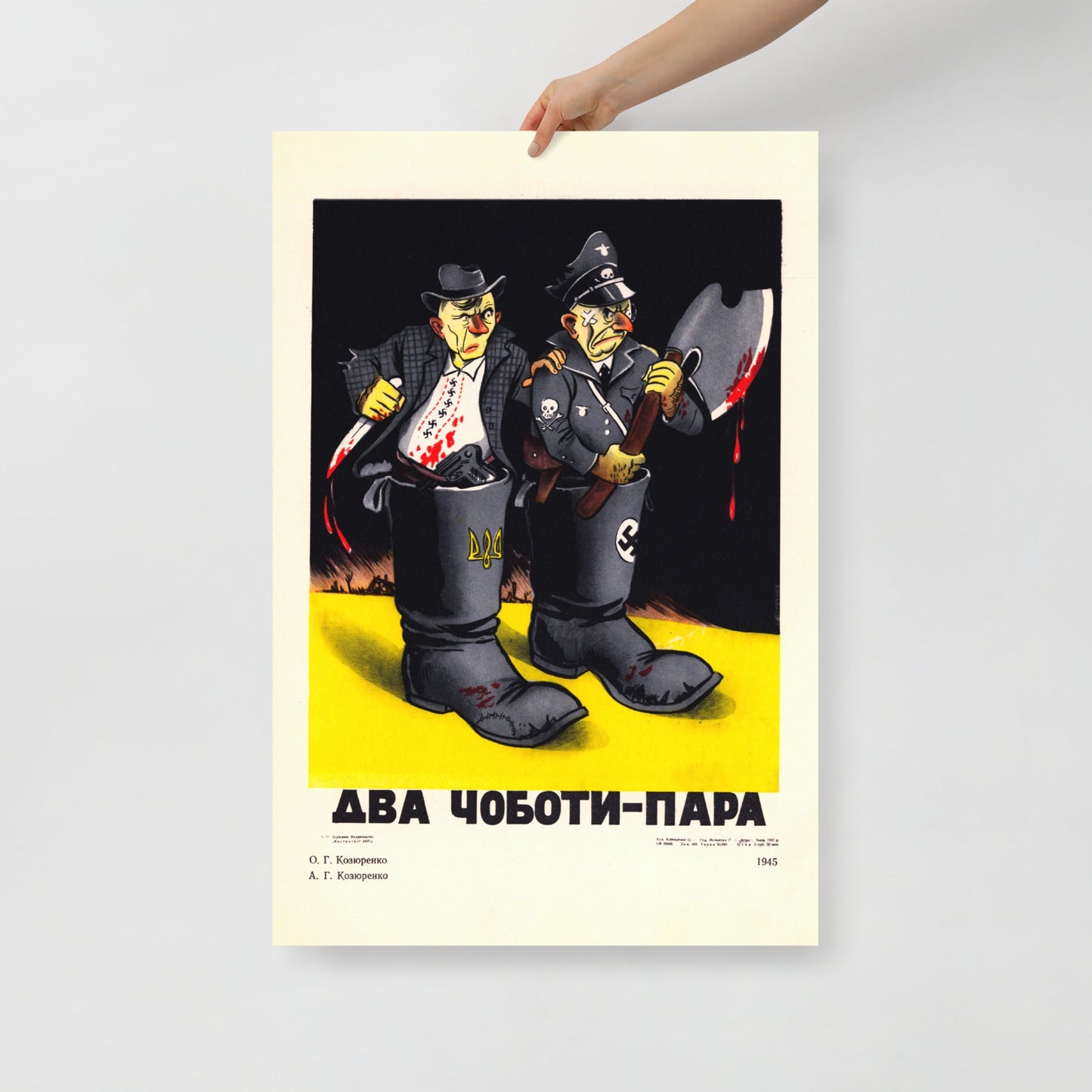 A hand holding large World War II Soviet propaganda poster showing Stepan Bandera with Ukrainian trident and Nazi militant with swastika in a boot, slogan “Two Boots — One Pair”. www.artsoviet.com