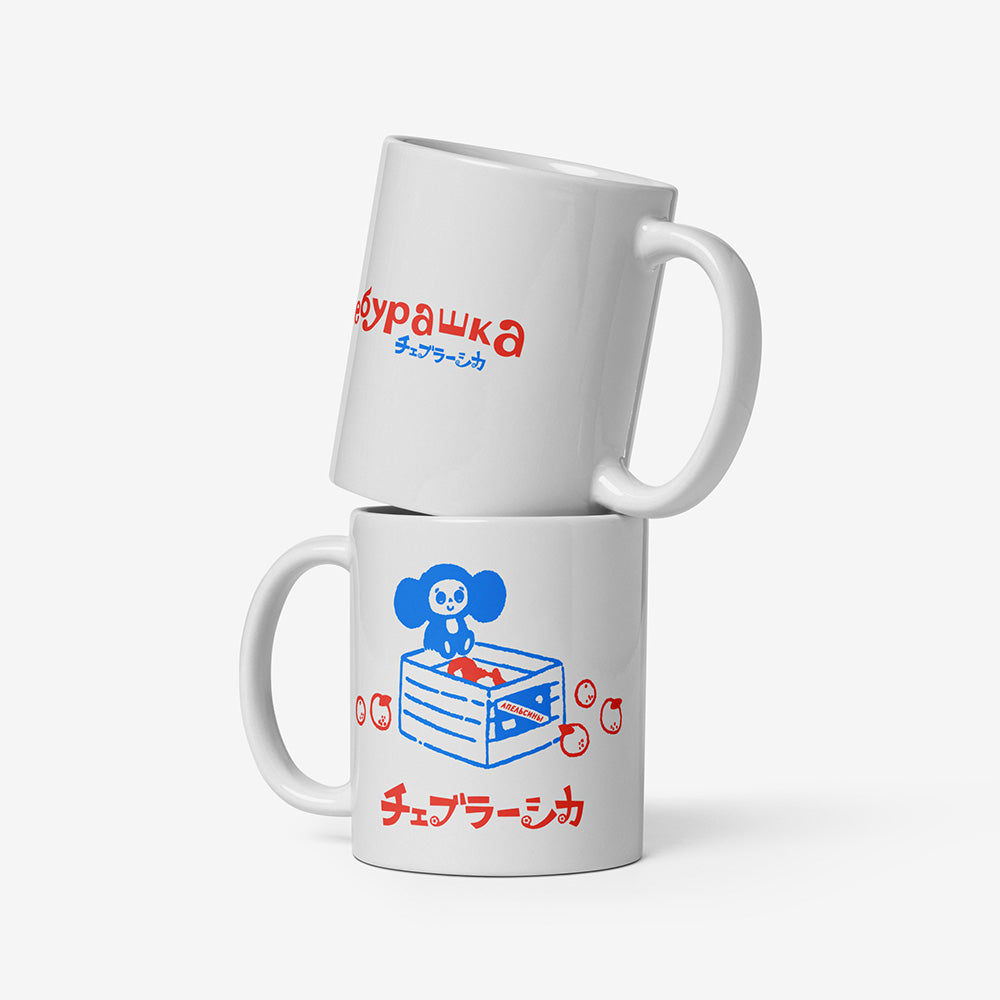 White ceramic mug with Soviet cartoon Cheburashka sitting on a box of oranges, and チェブラーシカ in Japanese below.