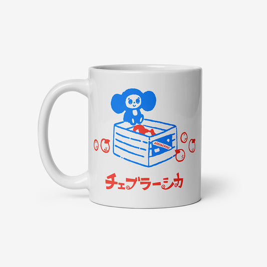 White ceramic mug with Soviet cartoon Cheburashka sitting on a box of oranges, and チェブラーシカ in Japanese below.
