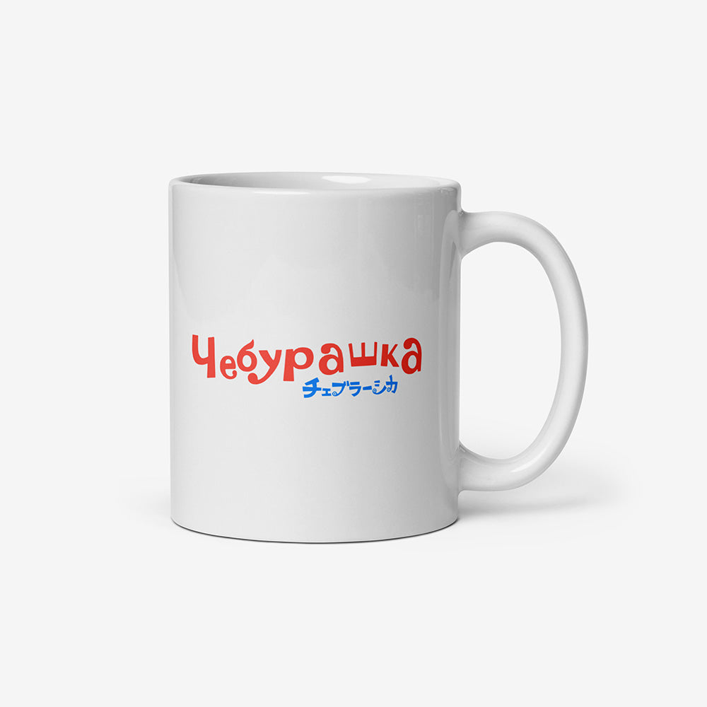 White ceramic mug with Soviet cartoon Cheburashka sitting on a box of oranges, and チェブラーシカ in Japanese below.