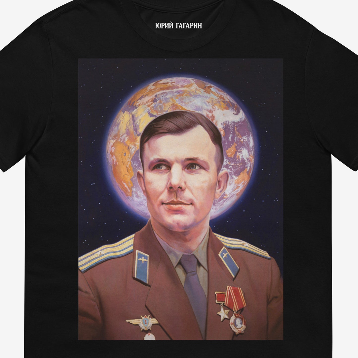 Black unisex T-shirt with large painting of Yuri Gagarin in medals, Earth halo behind head. Soviet space icon with Orthodox inspiration. Closeup print details photo with Юрий Гагарин logo in Cyrillic seen on the necktag. www.artsoviet.com